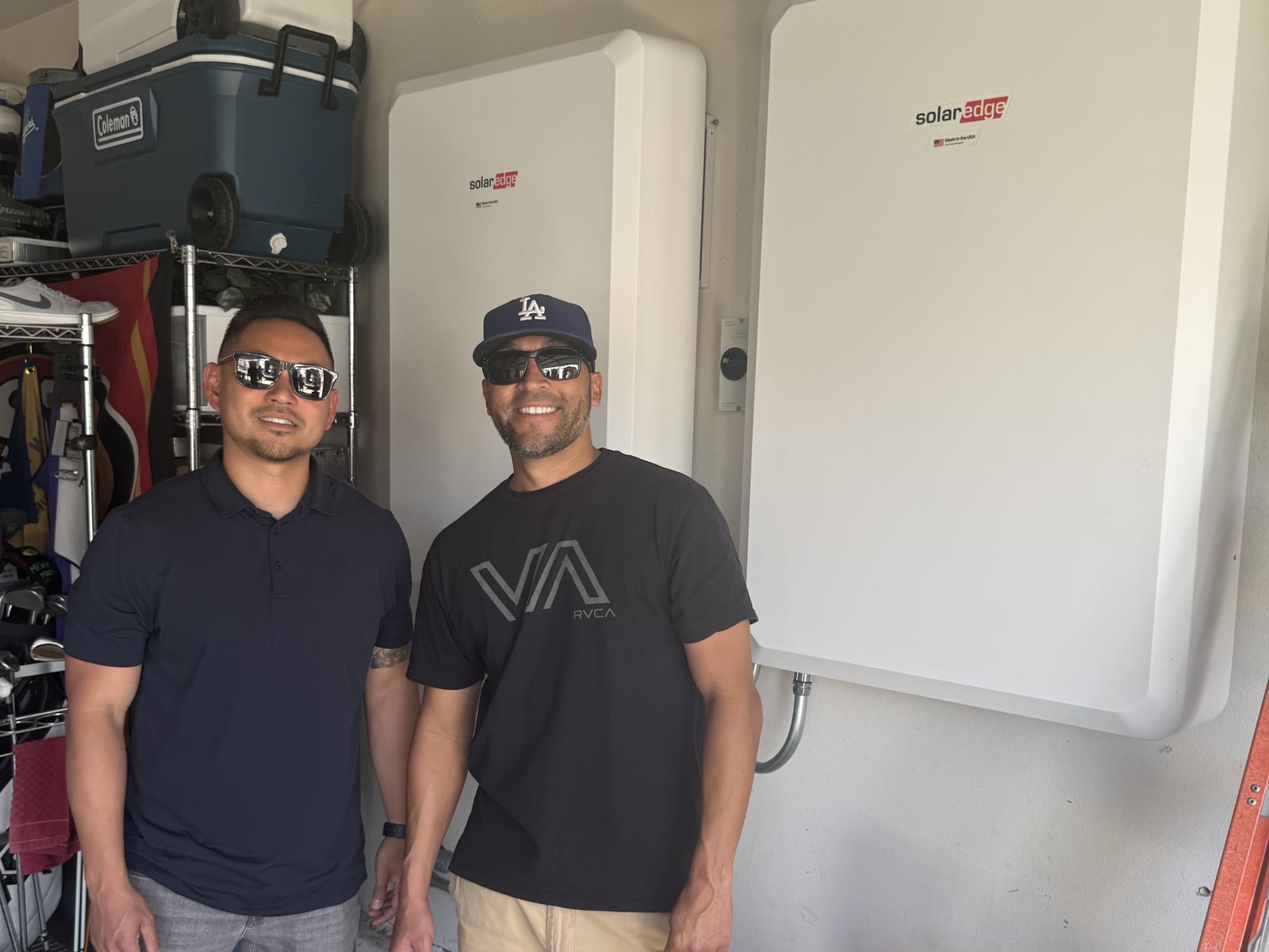 Two smiling men standing beside newly installed SolarEdge home batteries in a garage