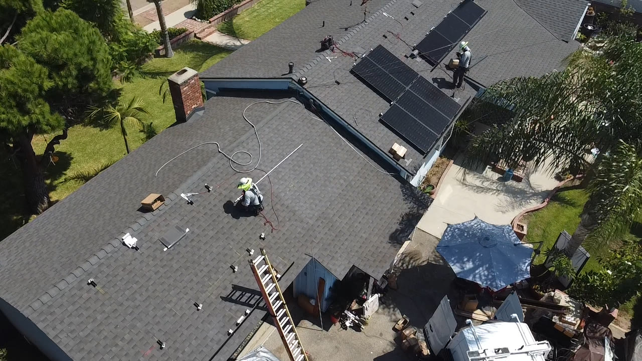 Installers setting black solar panels on a composition shingle roof
