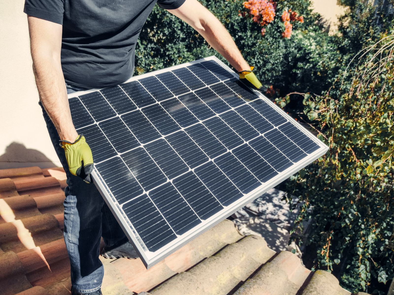 Installer carrying a solar panel across a tile roof